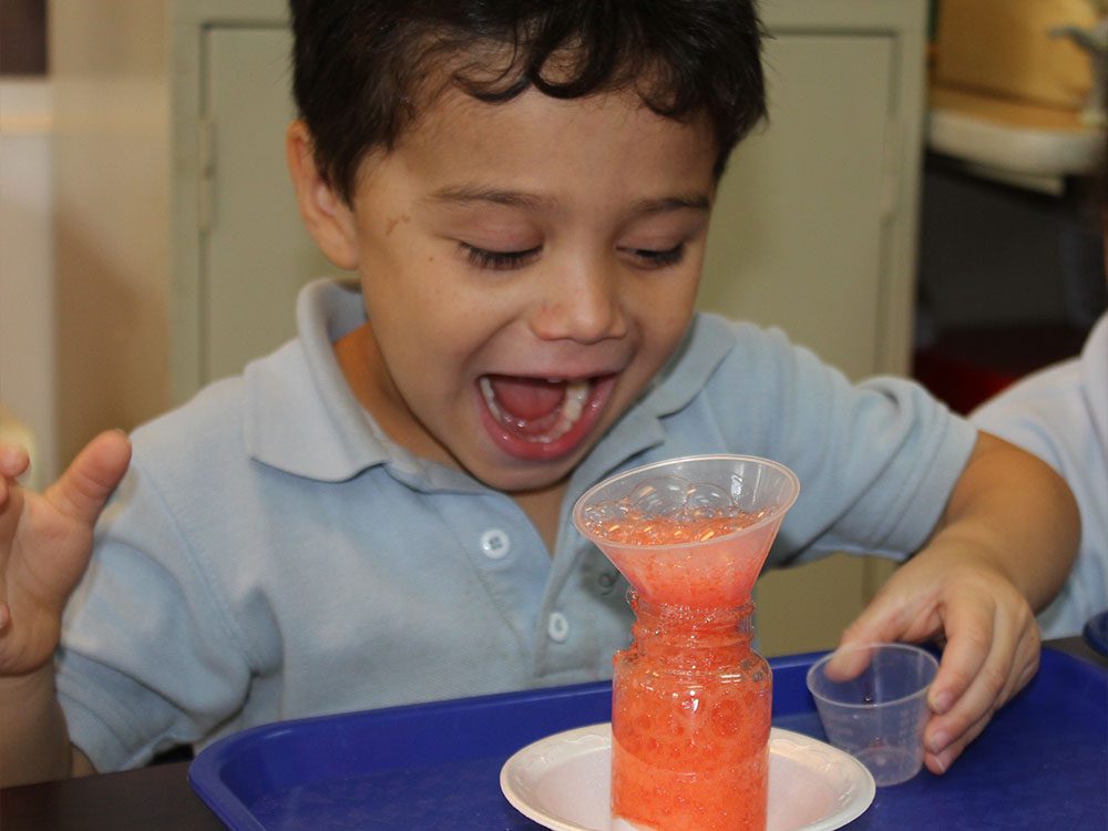 very happy and amazed little kid boy while looking at the bubbles created by colored soda at a Preschool & Daycare/Childcare Center serving Miami, FL.