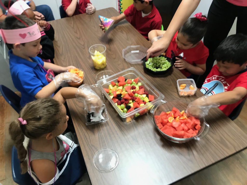 Group of preschoolers having fun while eating cut fruits at a Preschool & Daycare/Childcare Center serving Miami, FL.