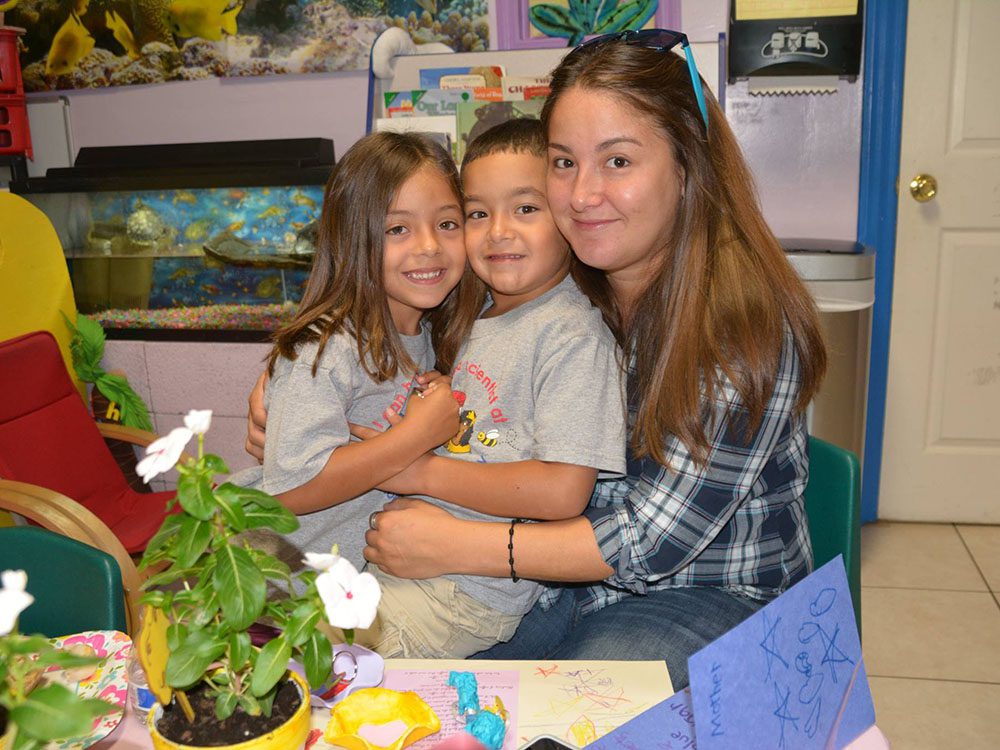 Happy mom and 2 little kiddos hugging each other at a Preschool & Daycare/Childcare Center serving Miami, FL.